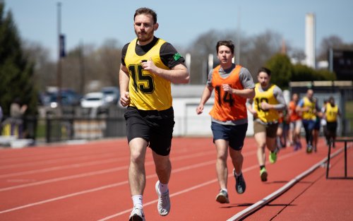 Students in yellow and orange jerseys run on the UAlbany track during the FBI physical fitness test.