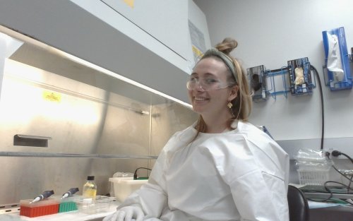 Rachel Lange sits at a lab lench in the Wadsworth Center. She wears protective gear.