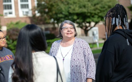 Victoria Rizzo smiles and speaks with three students outside on UAlbany’s Downtown Campus.