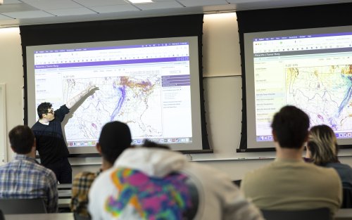 A UAlbany atmospheric science student points to a weather map of the United States.