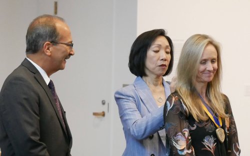 President Rodriguez looks on in delight, as Provost Kim places the Chancellor's Award medal around Allison Craig's neck.