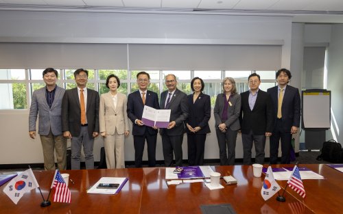 Nine people in business suits stand in front of a table topped with the American and South Korean flags and pose for a photograph