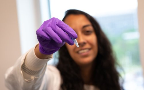 Sujata Murty holds up a crushed coral sample wearing a purple glove and lab coat.