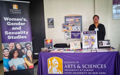 Dr. Janell Hobson is standing behind a table with a University at Albany Women's, Gener and Sexuality Studies banner, showcasing the University's Fall Preview event.