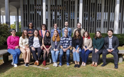 A diverse group of students stands in front of a building, smiling for a photo that highlights their unity and enthusiasm.