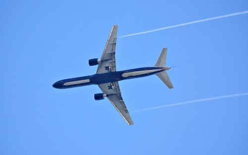Thin white clouds form behind a Boeing 757 on a clear sky day.