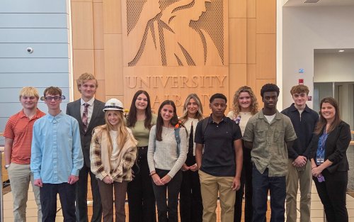 High school seniors from the New Visions program take a photo in front of the Minerva logo at ETEC.