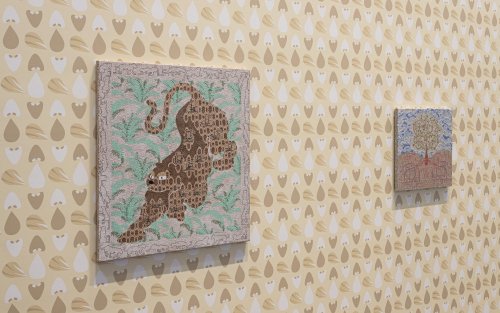 Two artpieces hang on a wall patterned with wall paper. One depicts a stylized tree and one a stylized panther.