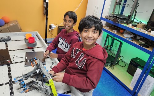 Two boys smile as they assemble a robot on a game board.