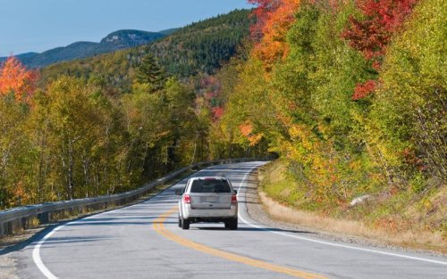 car is driving down the road surrounding by fall foliage