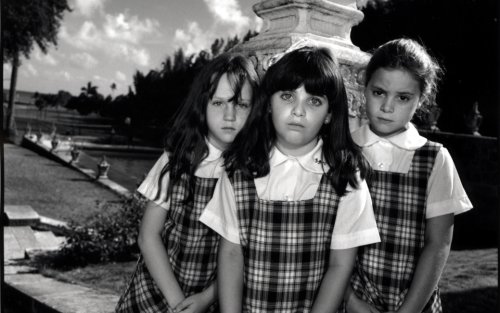 A black and white photo of three children standing in front of an old stone lantern. They are all wearing matching plaid dresses.