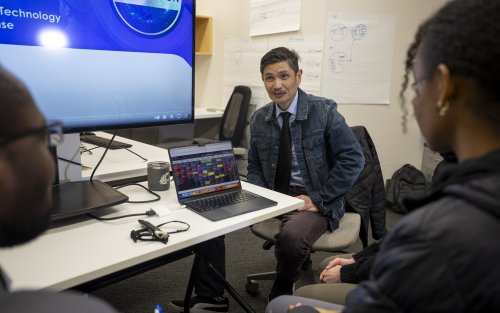 CEHC's Ariel Pinto meets with students while sitting next to a large screen and laptop.