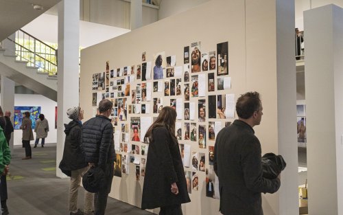 Visitors are walking around the first floor of the University Art Museum and are looking closely at a wall full of photographs and text by exhibiting MFA artist Hoora Mirabzadeh.