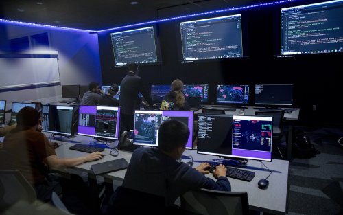 Students review code on a row of computers inside a dark lit room at ETEC.