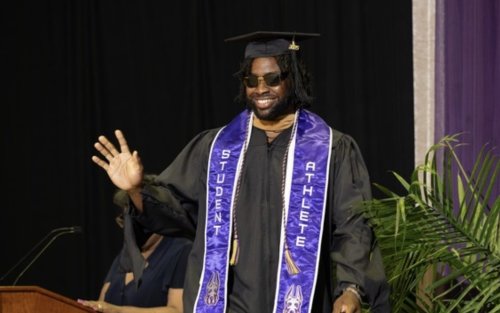 Student is wearing cap and gown, waving at the audience