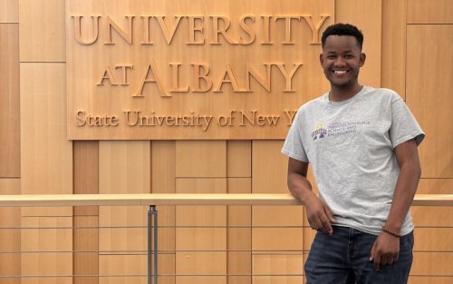 A smiling Emmanuel Kipchirchir stands in front of University at Albany sign.