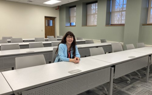 A smiling Mary Bayham sits in a row of seats inside a classroom. 