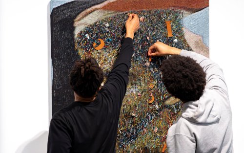 Two young African American students work with a fabric art piece in the University Art Museum by artist Noel W Anderson.
