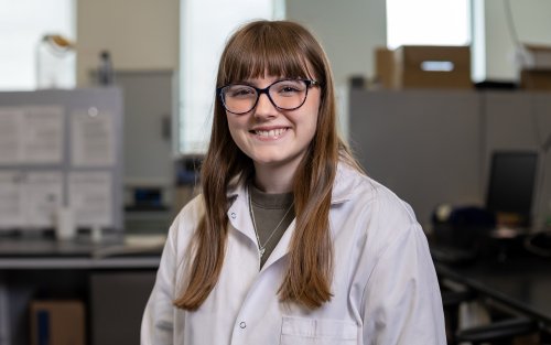 UAlbany undergraduate researcher Katelyn Jacques smiles while wearing a lab coat inside UAlbany's Paleoclimate Lab.