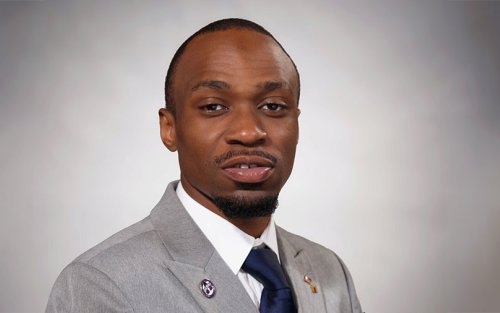 Christopher wearing a gray suit with a UAlbany pin.