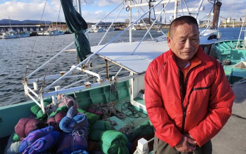 Haruo Ono a weathered man from Japan stands in front of his fishing trawler at Shinchi harbor, Fukushima.