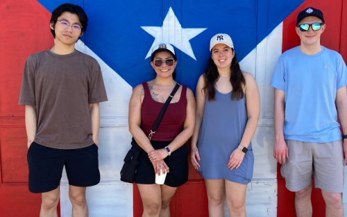 UAlbany students stand for a photo in front of a painting of the Puerto Rican flag.