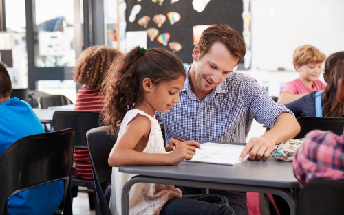 A teacher showing something on a piece of paper to a young child.