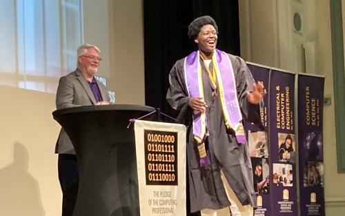 Woman in graduation robe smiles after receiving a computer science pin from her department chair.