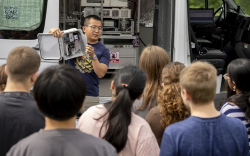 ASRC's Jie Zhang holds up instrumentation used in the mobile lab in front of Lisha Kill middle school.