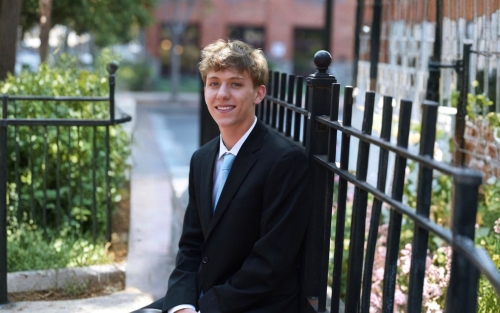 A smiling Brian Allen is dressed in a dark suit and seated outside.