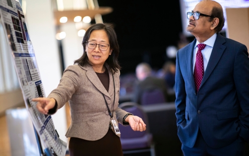 A faculty member points to her research poster while conversing with UAlbany Vice President for Research & Economic Development Thenkurussi (Kesh) Kesavadas.