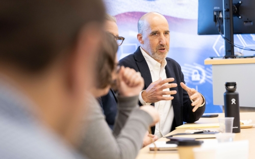 A researcher sitting at a table with other R&E Week 2024 attendees gestures with his hands while speaking.