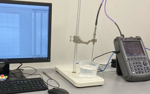 A monitor with unreadable data outputs sits next to lab equipment on a light gray tabletop