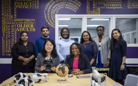 two women sit at a table with a globe and VR devices, while 6 others stand behind them
