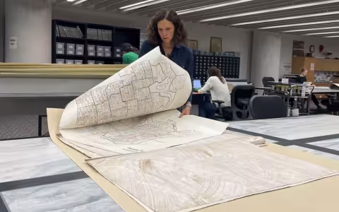 Samantha Friedman standing at a table folding a large white map with boxes on it depicting the neighborhoods of a city.