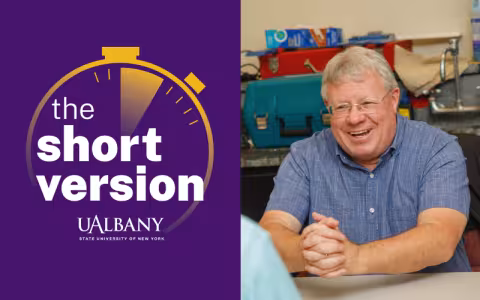 A split image with words "the short version" on the left surrounded by a gold stopwatch logo against a purple background and a smiling photo of a man in a blue button-down shirt on the right.