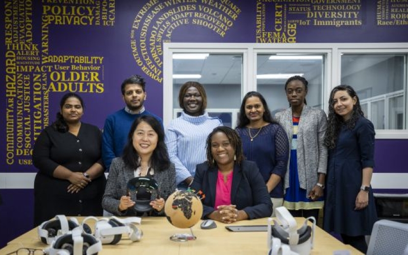 two women sit at a table with a globe and VR devices, while 6 others stand behind them
