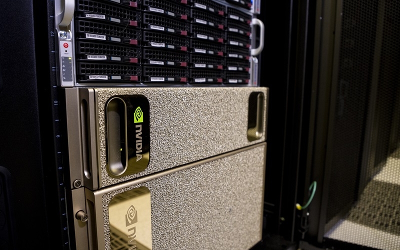 A close-up of a silver rectangular GPU system installed in a row of tall, black server racks. 