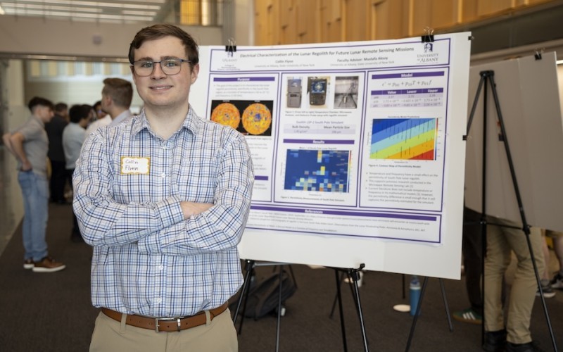 A young male student poses with a research poster at ETEC