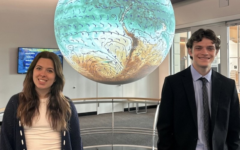 UAlbany students Micaela Maywald and Michael Miller stand in front of the Science-on-a-Sphere globe at ETEC.
