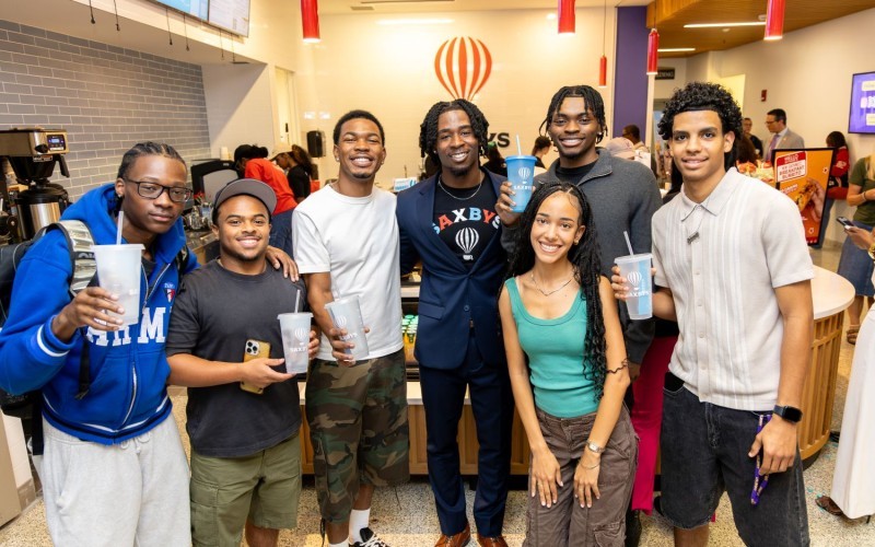 A group of students hold drinks while standing in front of a cafe inside the Massry School of Business at UAlbany