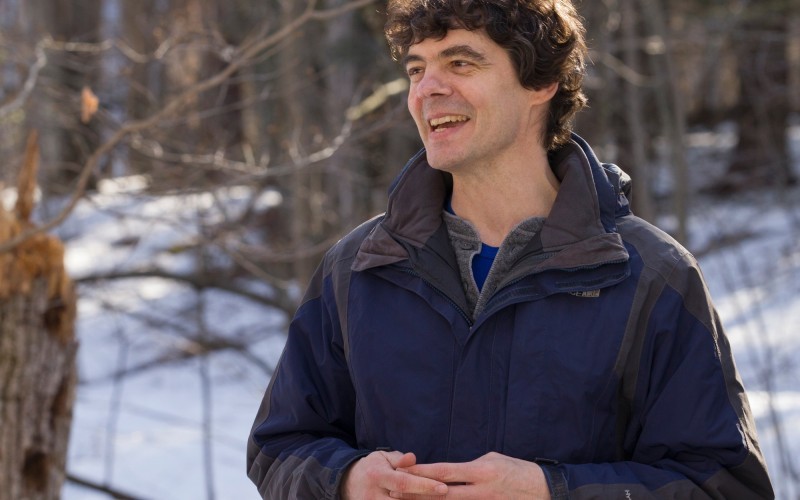Mathias Vuille stands in a wooded area on campus during the winter season.