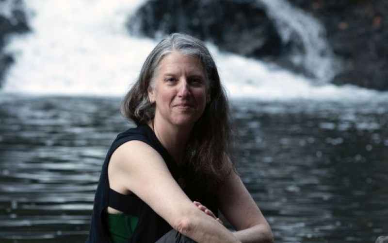 A woman sits on a rock with a stream and waterfall behind her.