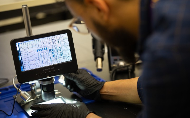 A man wearing black gloves shines a light while using lab equipment