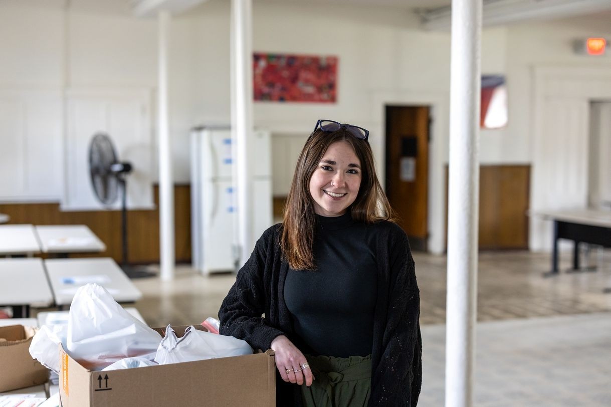 A woman poses for a portrait with her arm propped on a cardboard box filled with full plastic bags. 