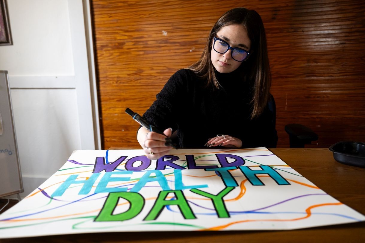 A woman outlines block text on a handpainted sign that reads "World Health Day"