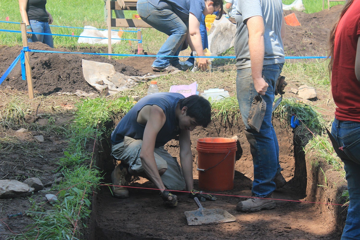 a person digging in a square hole for artificates with a bucket next to him and a sweep pan