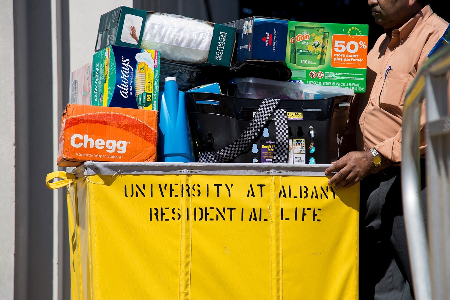 A man pushes a yellow rolling bin labeled "University at Albany Residential Life" that is full of a student's belongings