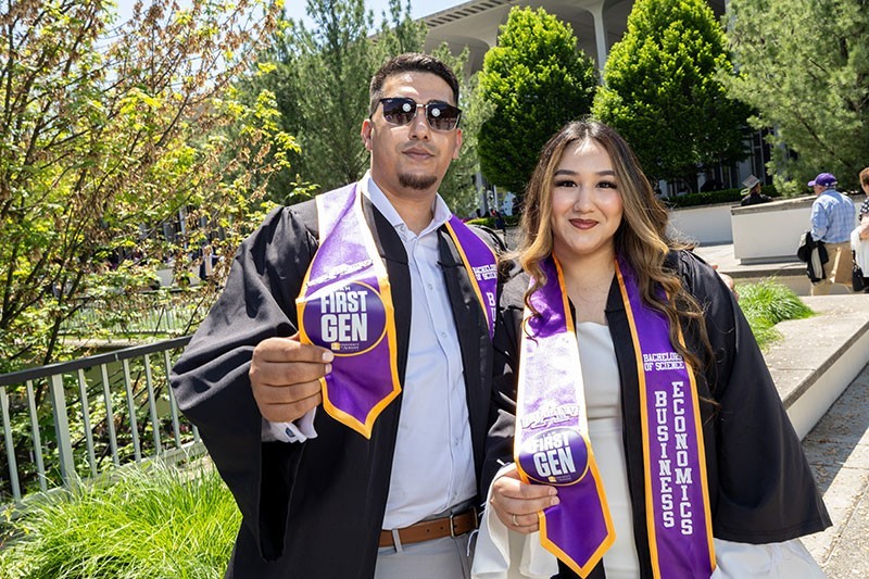 Two students at commencement holding sashes indicating they were first generation college graduates. 