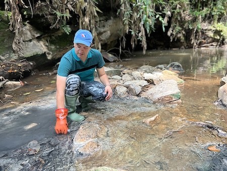 A man in boots and gloves takes a sample of river water in the rainforest